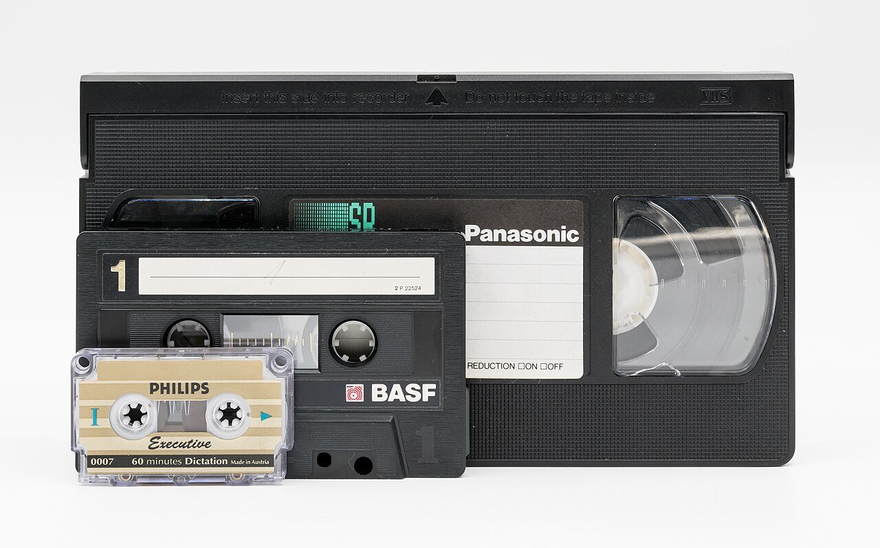 A VHS cassette tape next to a videocassette recorder