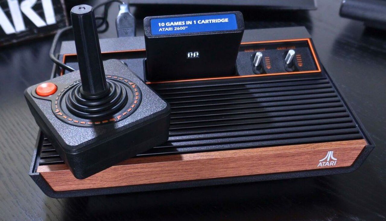 The Atari 2600+ console with a wood-grain front panel, a joystick and a bundled game cartridge