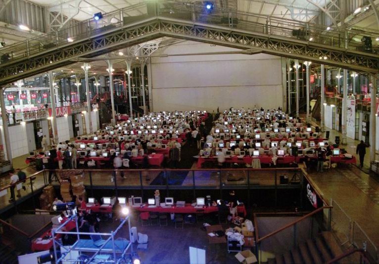 Rows of desktop computers and monitors set up on long tables at a LAN party